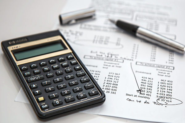 A finacial calculator and pen sit atop a sheet a sheet of calculations. Public domain image by PIXNIO.com user stevepb